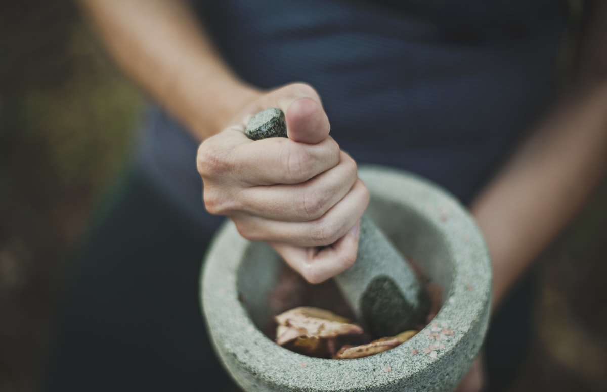 Hands grinding whole spices in a stone mortar and pestle
